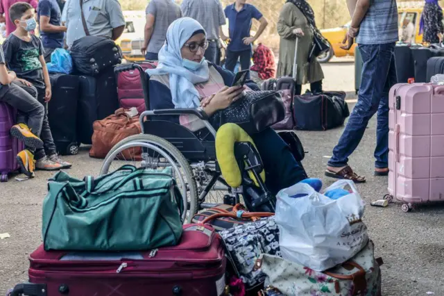 سيدة تجلس على كرسي متحرك وتنتظر دورها في معبر رفح، ترتدي هو طفل خلفها كمامة، يظهر أن الصورة أُخذت وقت انتشار كوفيد 19