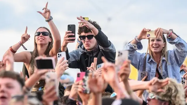 Tłum na festiwalu muzycznym. Trzech fanów siedzi na ramionach innych.