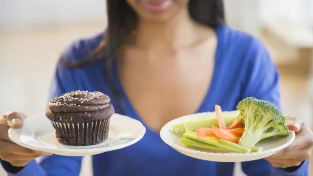 Mulher segurando um prato com legumes e outro com cupcake