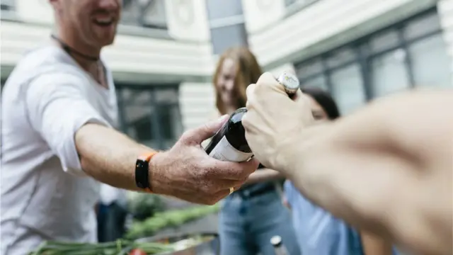 Un hombre pasándole una cerveza a otro.