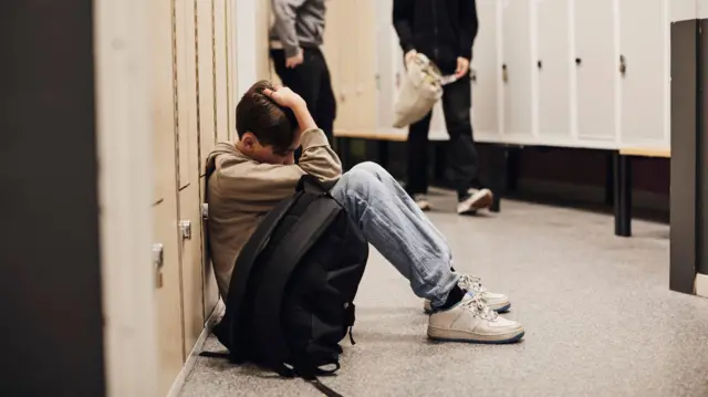 ጭንቀት ውስጥ ያለ ልጅ አቀርቅሮ ቦርሳውን እንደያዘ መሬት ላይ ተቀምጦ