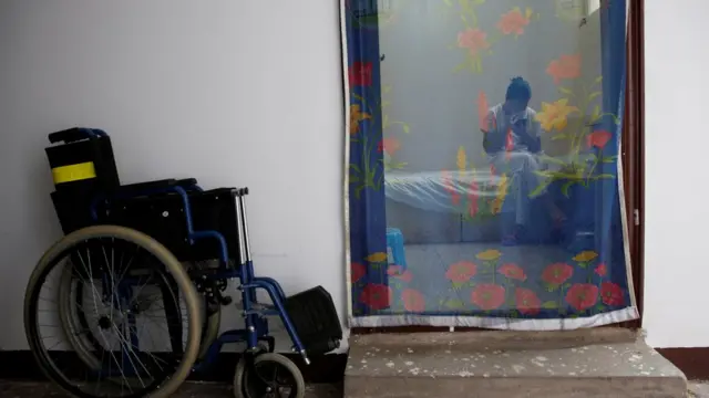 Mujer revisa su teléfono celular detrás de una cortina que hace las veces de puerta.