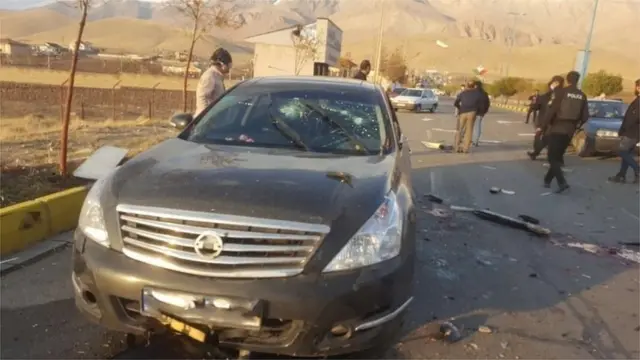 Foto do carro do cientista após o ataque, com os vidros rachados e danos causados por aparente explosão