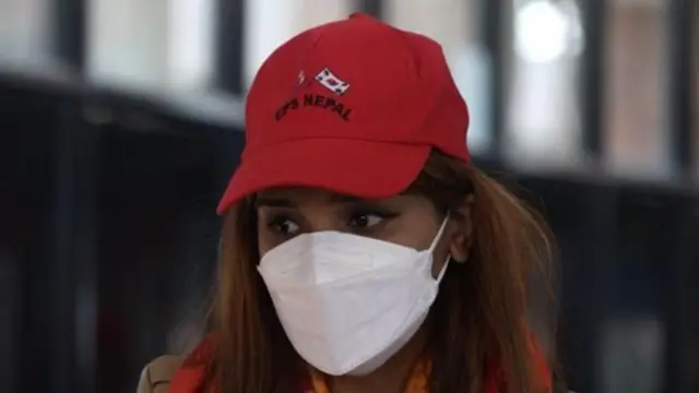 इपिएस नेपाल लेखिएको रातो क्याप लगाएकी र मुखमा मास्क लगाएकी महिलाको तस्बिर