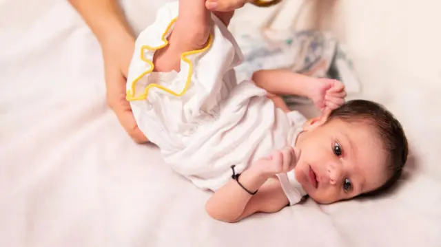 Close-up of a mother dressing her newborn baby on white bed.