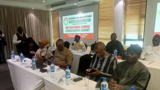 Aworan awọn olukopa nibi ipade Eko naa lasiko to n lọ lọwọ. Wọn wa nijokoo, omi wa lori tabilu bẹẹ ni ọkunrin kan duro pẹlu ohun to gbe dani