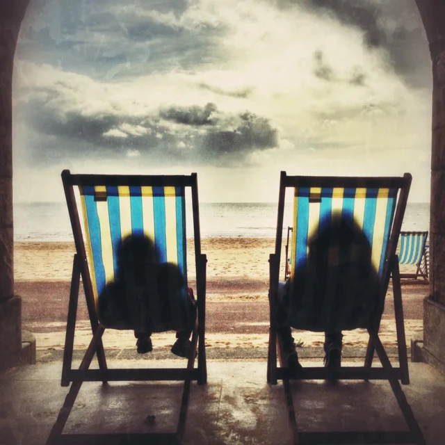 Sombras de duas pessoas em cadeiras de praia de frente para o mar