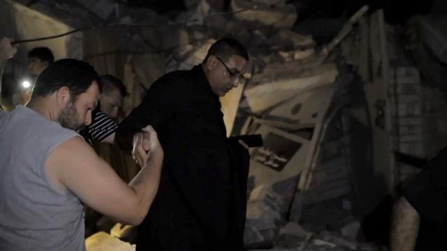 Спасатель держит за руку выжившего человека, выбирающегося из-под завалов