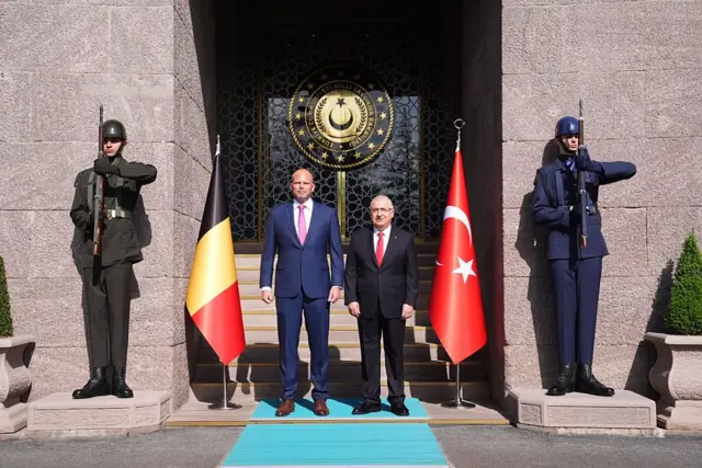 İki bakan, bakanlık girişinde yan yanalar. Yanlarında iki türk askeri selam duruyor.