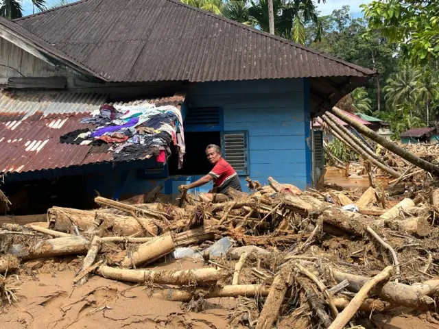 Seorang warga di Hutanabolon sedang membersihkan rumahnya dari tumpukan kayu dan lumpur yang dibawa banjir bandang.