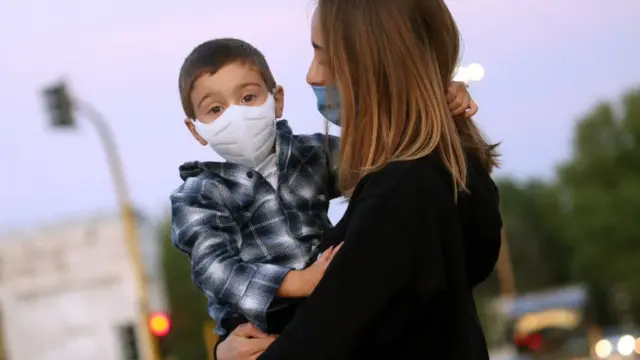 Mãe com o filho no colo, ambos com máscaras