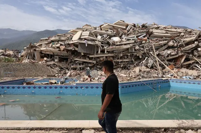 சேதமடைந்த கட்டடக்குவியலைப் பார்த்தவாறே கடந்து செல்லும் கராகஸ் நகரவாசி