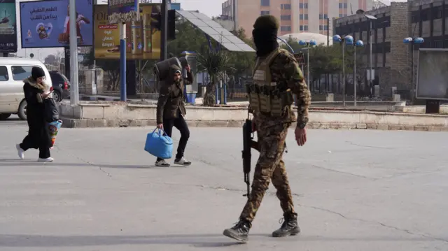 یک عضو ارتش سوریه، در حالی که غیرنظامیان در پی درگیری‌های مجدد میان ارتش سوریه و نیروهای دموکراتیک سوریه (SDF) در حال فرار هستند، با سلاحی در دست در یک سرک حلب قدم می‌زند.