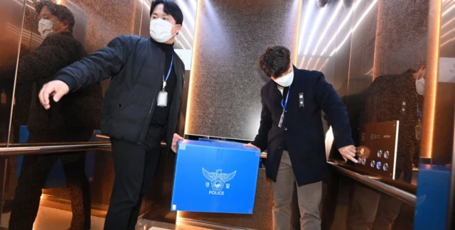 Polis, havalimanının idari ofislerinde yapılan arama sonrası el koyulan belgeleri asansöre bindiriyor. Mavi bir kutunun üzerinde polis yazıyor.