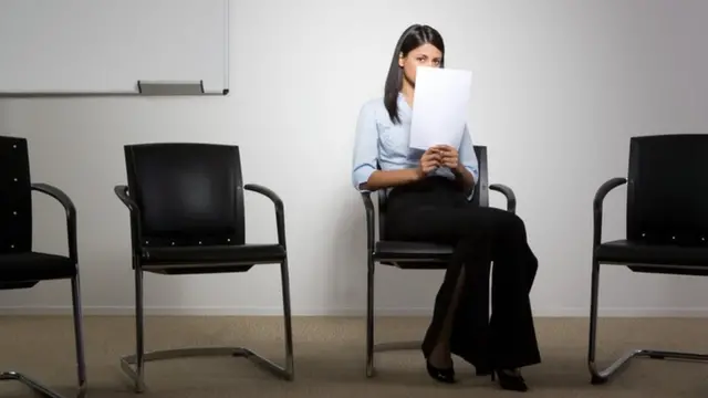 Una personas sentada, cubriéndose el rostro con unos papeles