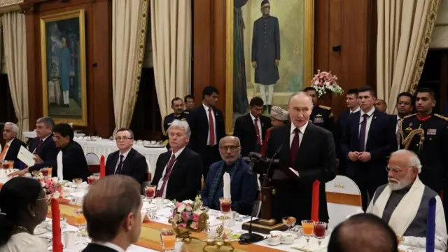 花や複数の食器、ナプキンなどで整えられた夕食会用の長いテーブルに、インドとロシアの両政府代表が並んで座っている。ロシアのドミトリー・ペスコフ大統領報道官、インドのドルパディ・ムルム大統領も座っている。複数の側近が後ろに立ち、茶色い木製の壁にはさまざまなインド政治家の大きい肖像画がかかっている