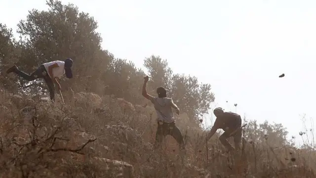 صورة تُظهر مستوطنين ملثمين وهم يحملون العصي ويرشقون الحجارة في بلدة بيتا بمدينة نابلس في الضفة الغربية