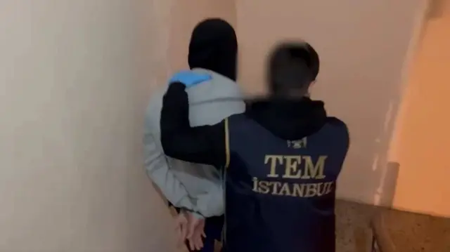 IŞİD operasyonunda bir polis bir şüpheliyi ters kelepçeli bir şekilde götürüyor.