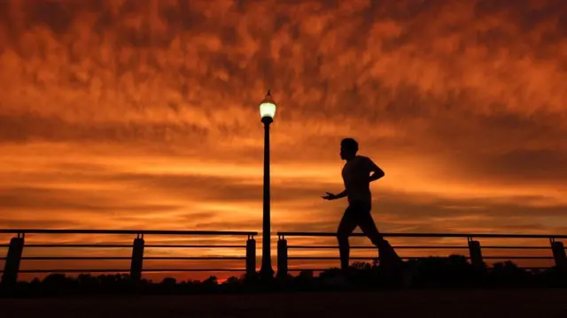Pessoa correndo com céu laranja, de por do sol, ao fundo