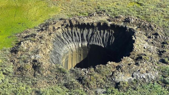 Imagem da crateca no ártico, um buraco enorme com as bordas que parecem formadas por explosão e com vegetação baixa em volta