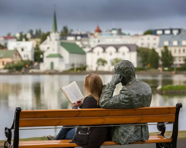 Mulher lendo ao ladojumba bet sign up bonusestátua do peta islandês Tomas Gudmundssonjumba bet sign up bonusReykjavik, Islandia.