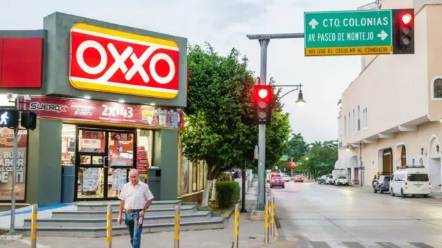 Un hombre pasa por delante de una tienda de Oxxo con su letras blancas sobre rojo en una esquina de la ciudad de Mérida.