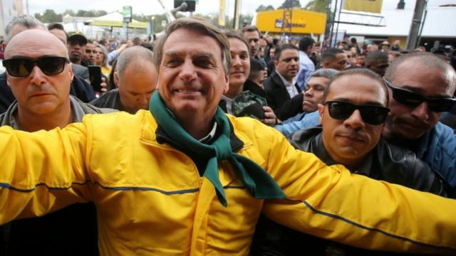 Bolsonaro sorrindo com vestimentasbet 365 dota 2verde e amarelo rodeado por seguranças e apoiadores nas ruas