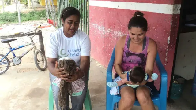 visitadora do criança feliz segura boneca no colo (esq) e mãe segura filho da mesma forma (dir)