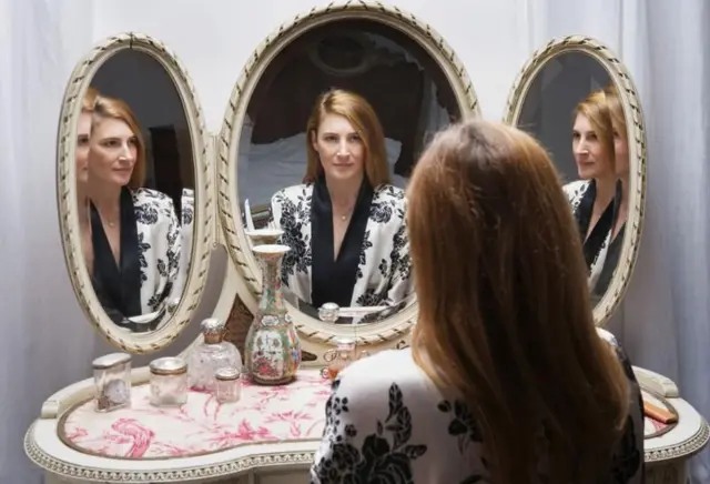 Mulher branca jovem olhando seu próprio reflexo em três espelhos