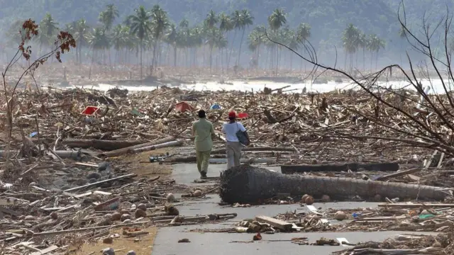 Dua pengungsi berjalan menyusuri jalan yang dipenuhi puing-puing sisa bencana tsunami saat mereka kembali mencari rumah di kota pantai barat Leupung, sekitar 30 km dari Banda Aceh, pada 9 Januari 2005.