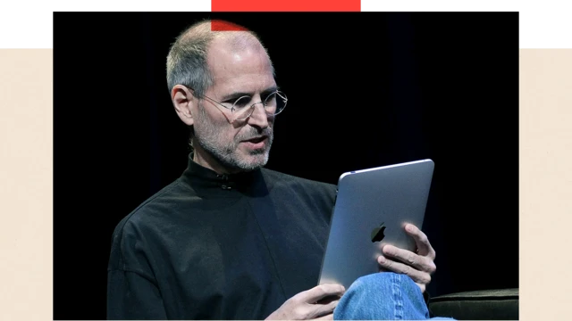 Steve Jobs egy iPad táglagépet tart a kezében, és azt nézi.
