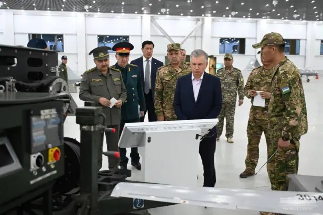 O'zbekiston prezidenti harbiy texnikani ko'zdan kechirayapti. Uning atrofida harbiy kiyim kiygan askarlar bor.