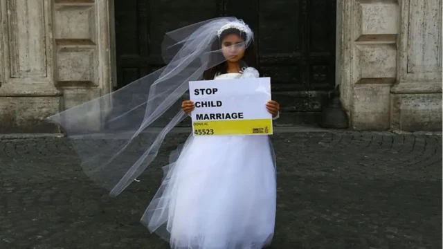 Seorang anak perempuan berbaju penganti sedang memegang poster antipernikahan anak.