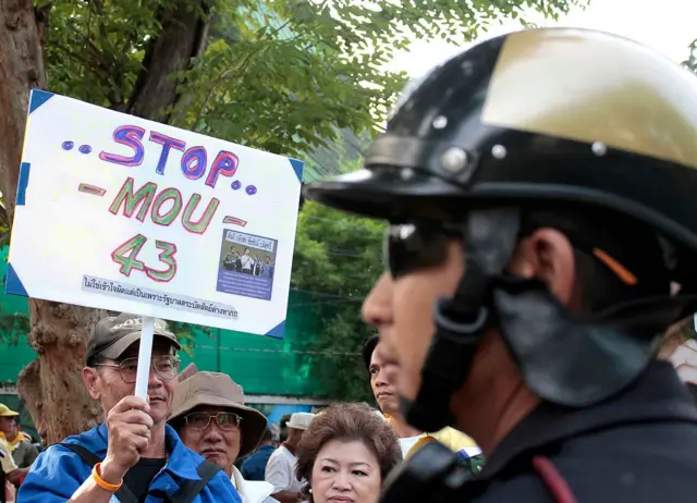 THAILAND OUT - A Thai policeman (R) stands guard as protesters hold signs during a rally outside the Parliament building in Bangkok on November 2, 2010. Some 1,000 People's Alliance for Democracy (PAD) supporters rallied outside the Parliament to protest against a proposed Thai-Cambodia Memorandum of Understanding (MOU) on their border demarcation. AFP PHOTO (Photo credit should read STR/AFP via Getty Images)