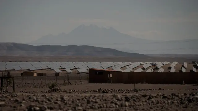 Una casas están enfrente de una larga fila de paneles solares que son parte de la planta solar Rubí. 