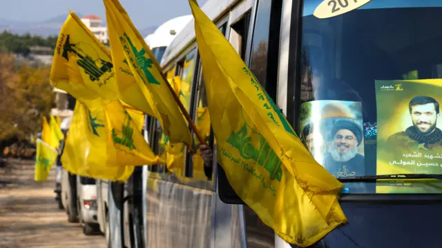 ဟစ်ဇ်ဘိုလာခေါင်းဆောင်း ဟာဆန် နာဆာရာလာပုံ ကပ်ထားတဲ့ ကားပေါ် မှာ အလံကိုင်ဆောင်ပြီး လိုက်ပါစီးနင်းလာတဲ့ ဒေသခံတွေ 