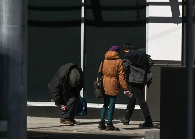 Hombre en la calle cabizbajo, con las rodillas flexionadas y los brazos caídos.