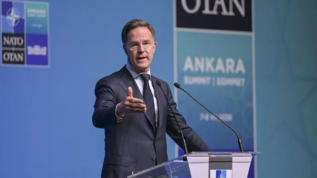 Rutte kürsüden basın mensuplarının sorularını yanıtlıyor. Arkasında NATO Ankara zirvesi logoları olan mavi bir arka plan var.