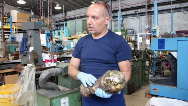 Funcionário manuseia réplica da taça da Copa