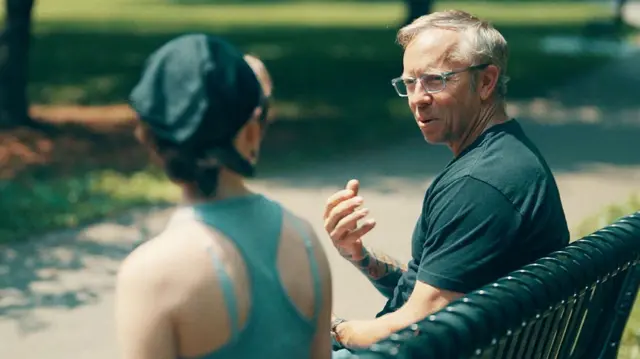 muškarac i žena sede na klupi u parku i razgovaraju