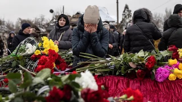 Жінка закрила обличчя руками перед труною з квітами