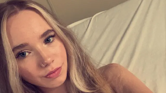 Megan Dixon é uma jovem loira com olhos claros e um piercing no nariz. Ela está deitada em um travesseiro e olhando para a câmera