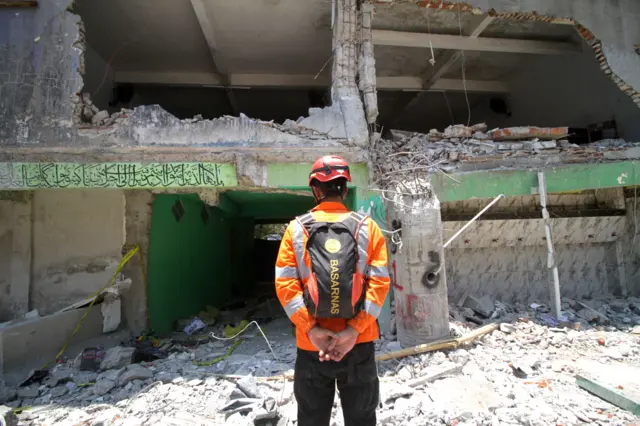 Anggota SAR berdiri di depan bangunan ambruk Ponpes Al Khoziny.