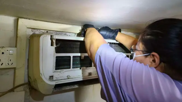 A woman in a purple shirt fixes an air conditioner.