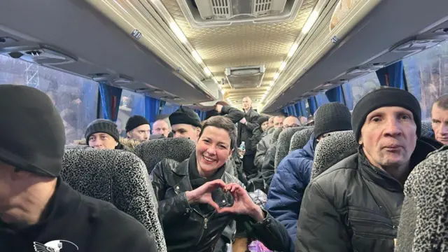 Освобожденные 13 декабря политзаключенные въехали на территорию Украины. Фото сделано в проходе автобуса, люди, одетые в черное, сидят по двое. Во втором ряду Мария Колесникова слегка наклоняется и показывает фотографу руки, сложенные в знак сердца