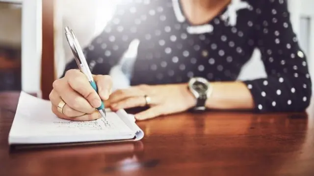 Mulher escrevendocaçaniquelcaderno sobre uma mesa