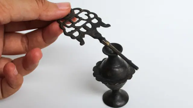 A women's hand holding an old make up tool for Kohl eyeliner, and an old storage cup.