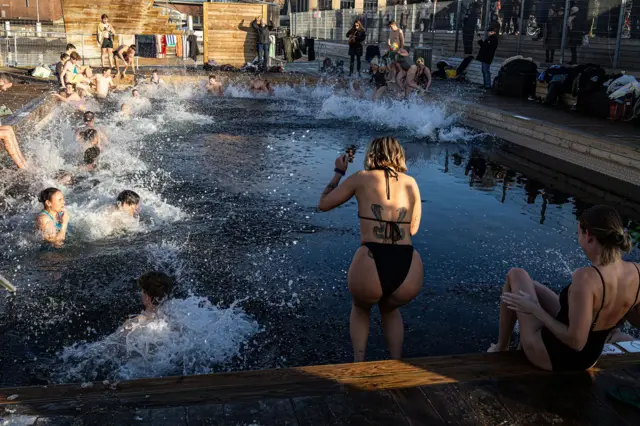 A group of people jumping in a cold water pool making a splash
