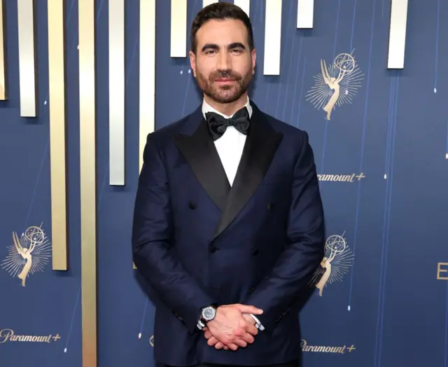 Glum Bret Goldstein u crnom odelu, beloj košulji sa crnom leptir mašnom