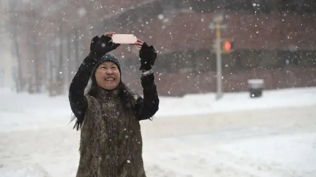 Seorang wanita tengah mengambil foto saat salju turun.